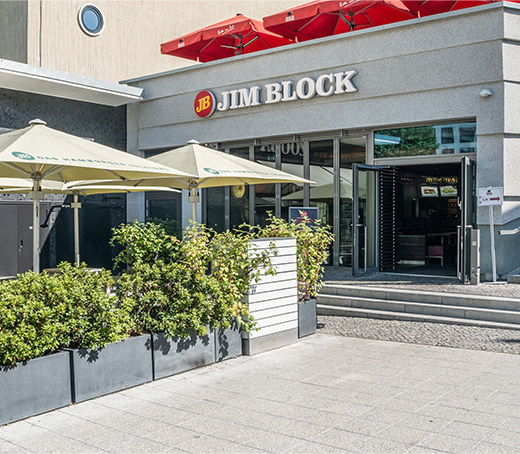 Eingang zum Jim Block Restaurant in Bikini-Berlin mit Sonnenschirmen und Pflanzenkübeln.
