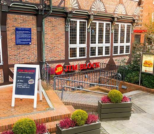 Eingangsbereich des Jim Block Restaurants in Bergedorf mit Aufsteller, Pflanzen und Ziegelmauer.