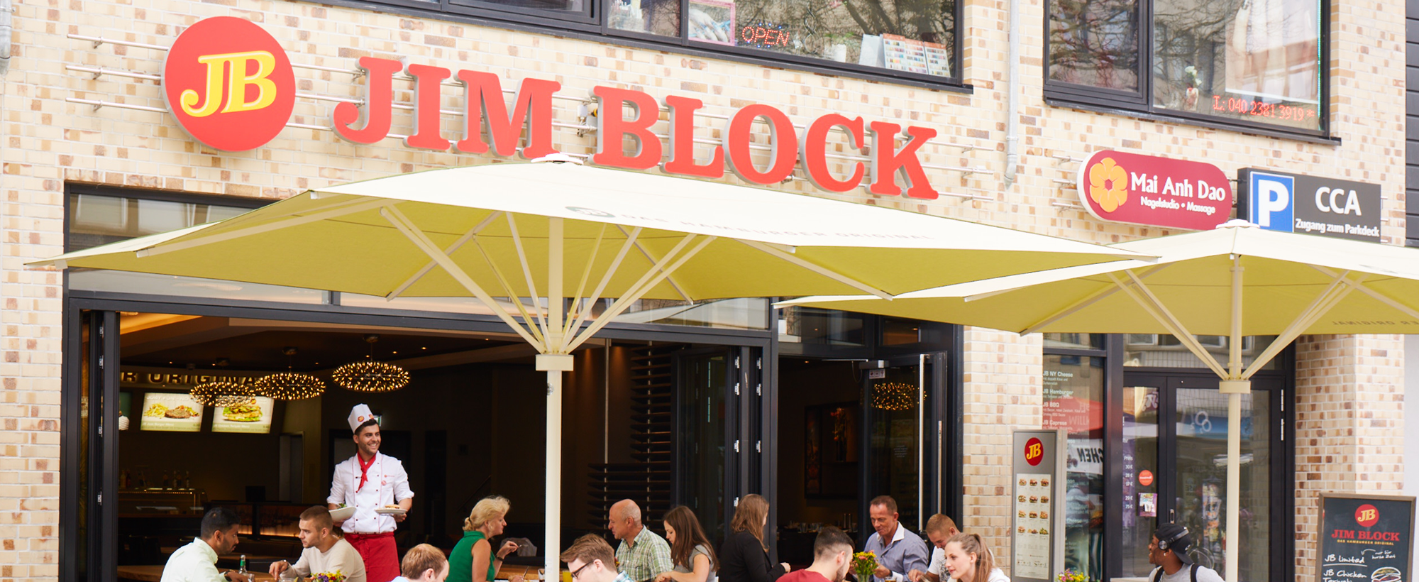 Jim Block Filiale in Altona mit Gästen Jim Block Filiale in Altona mit Gästen unter großen Sonnenschirmen im Außenbereich.
