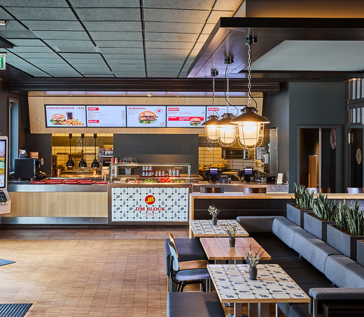 Innenansicht des Jim Block Restaurants in Othmarschen mit modernen Sitzbereichen und digitaler Menütafel über dem Bestellcounter.