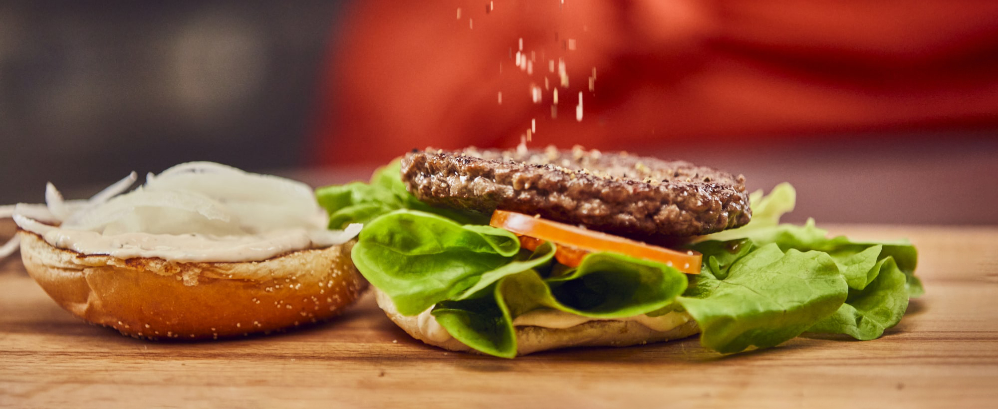 Jim Block Burger Zubereitung Frisch belegter Burger mit Patty, Salat, Tomate und Sesambrötchen in der Zubereitung.